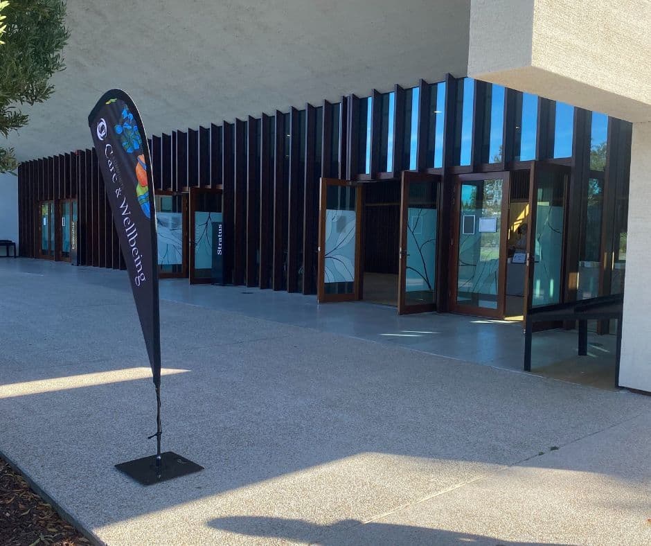 The entrance to a building with a Community Care and Wellbeing flag outside.