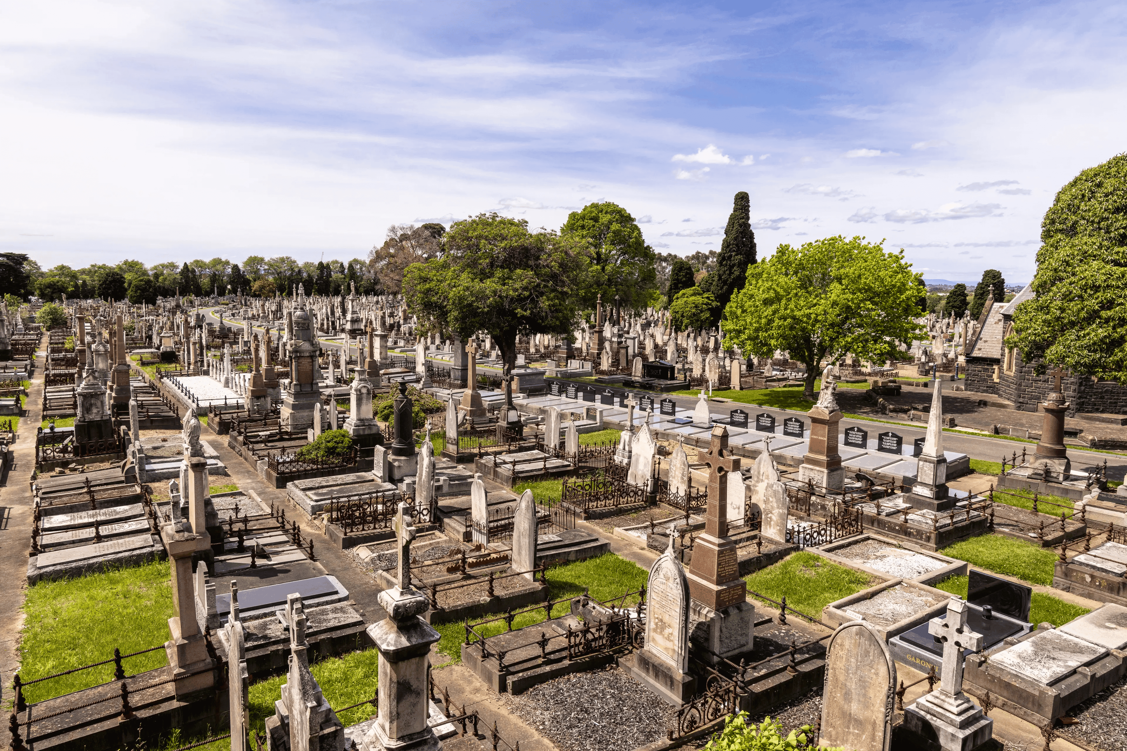 A cemetery filled with various graves, shaded by trees, offering a quiet space for reflection and honouring the deceased.