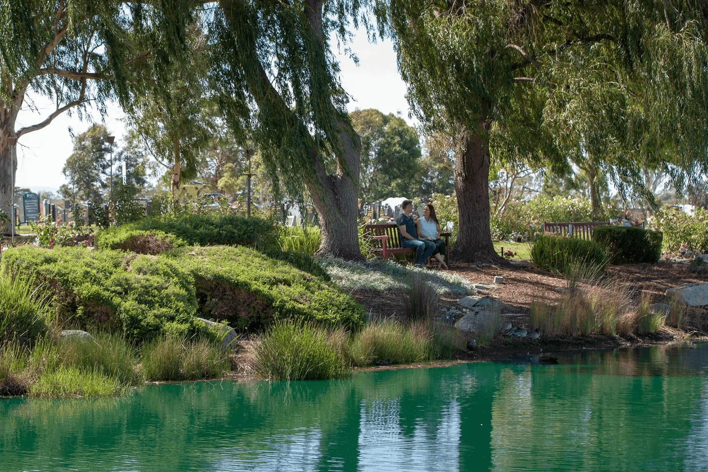 Couple sitting peacefully by a tranquil lake in a memorial park, surrounded by nature and reflecting in a serene setting