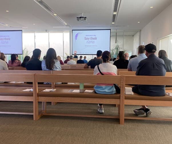 A group of people sitting at a remembrance event, photographed from the back.